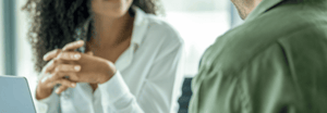 A woman with her hands folded sitting across from a man
